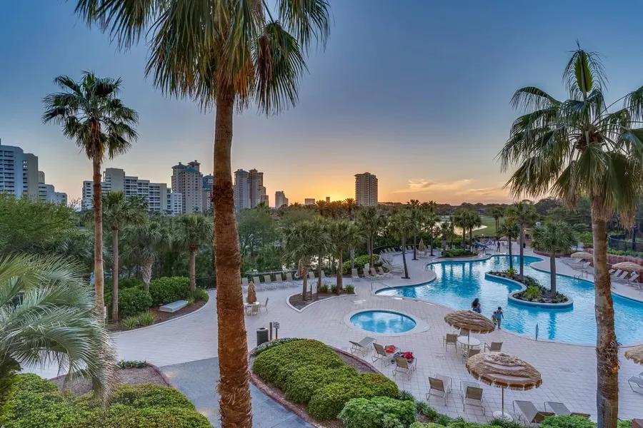 Palm-lined resort pool and hot tub with condo skyline at sunset