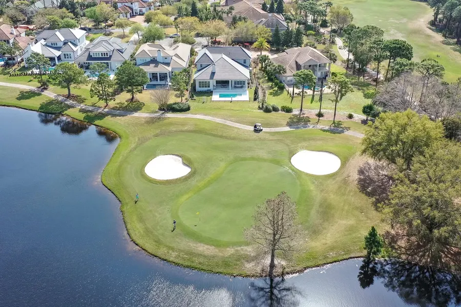 Aerial view of golf green with bunkers and luxury homes beyond a pond