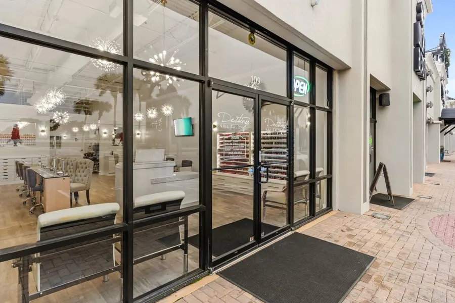 Glass storefront entrance of a bright nail salon on a brick walkway