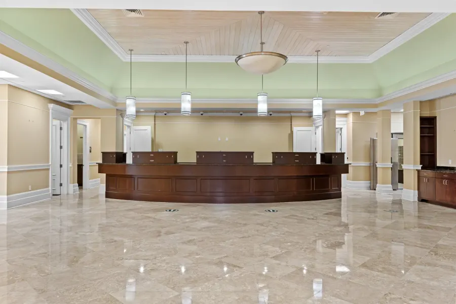 Grand curved wood reception desk under pendant lights on marble floor