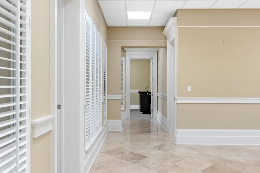 Travertine-floored office hallway with plantation shutters and crown molding
