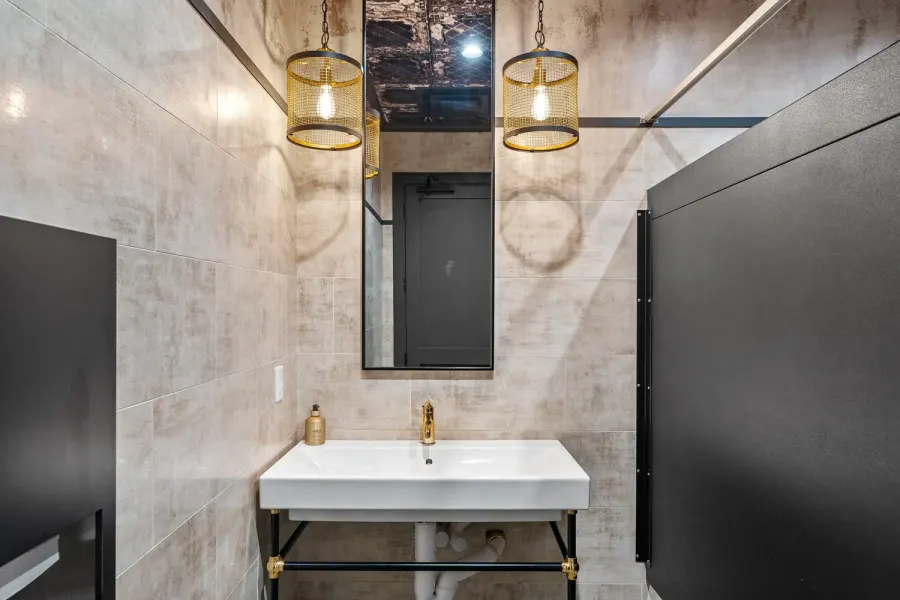 Industrial-chic restroom with brass pendant lights and white trough sink