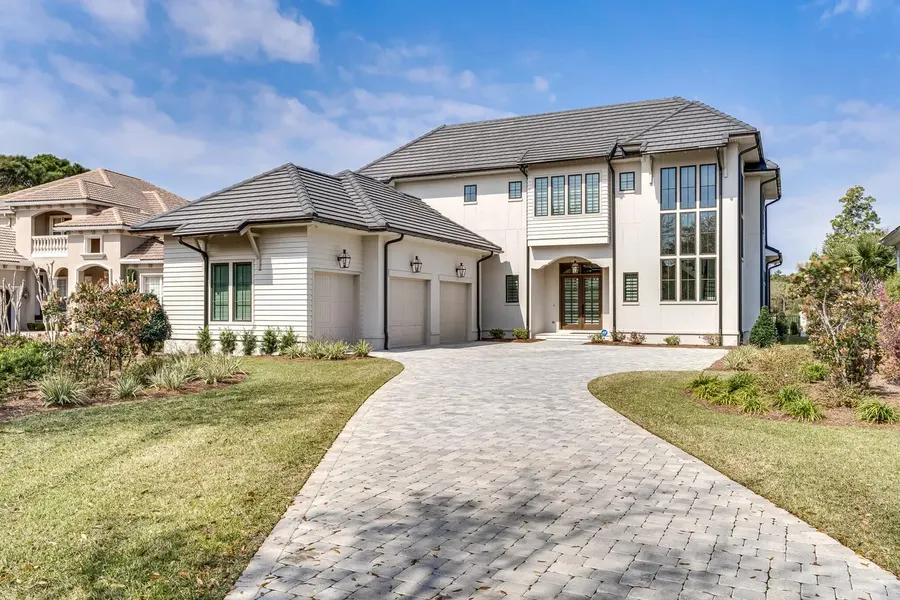 Two-story coastal home exterior with three-car garage and paver driveway