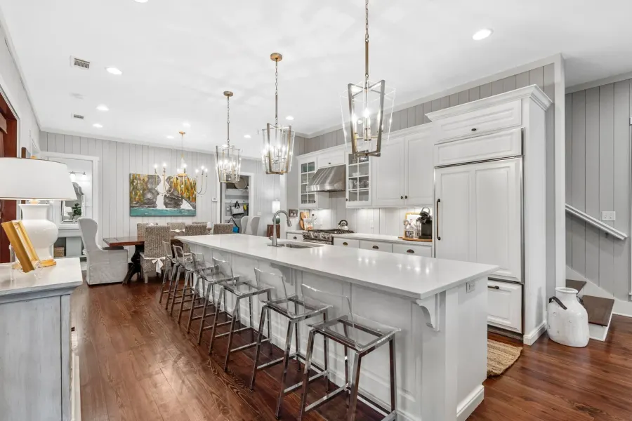 White kitchen with long island, lantern pendants, and acrylic barstools
