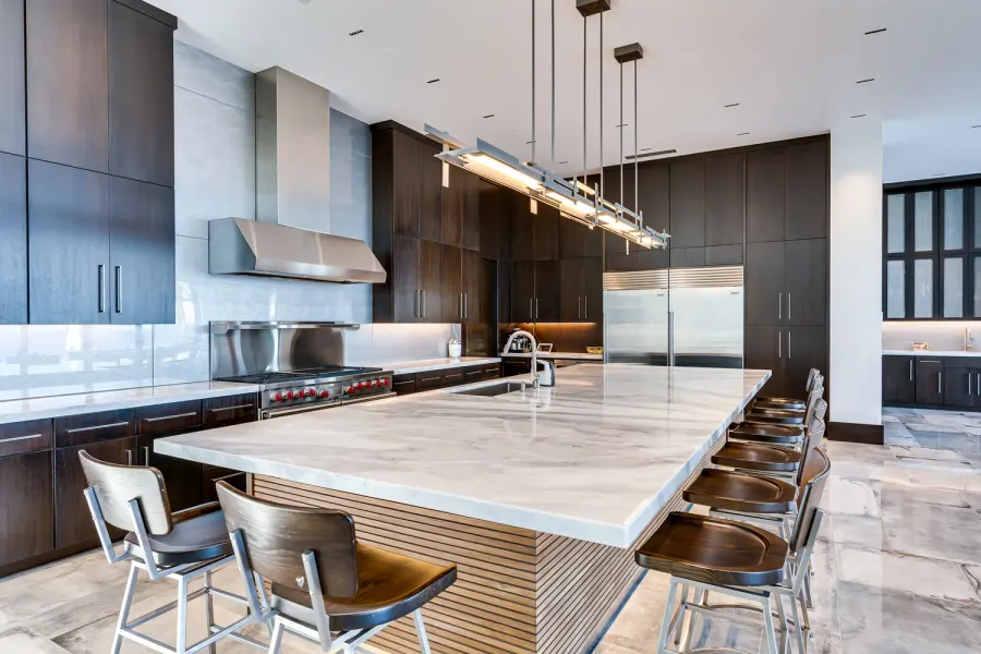 Sleek kitchen with marble waterfall island, dark cabinetry, and linear lighting