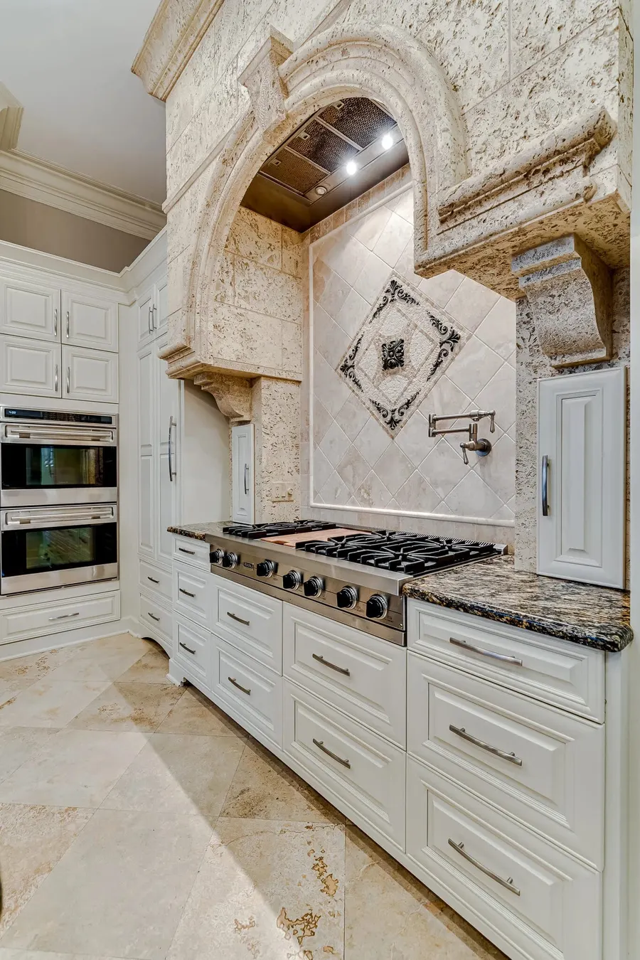 Ornate stone range hood over professional gas cooktop in luxury kitchen