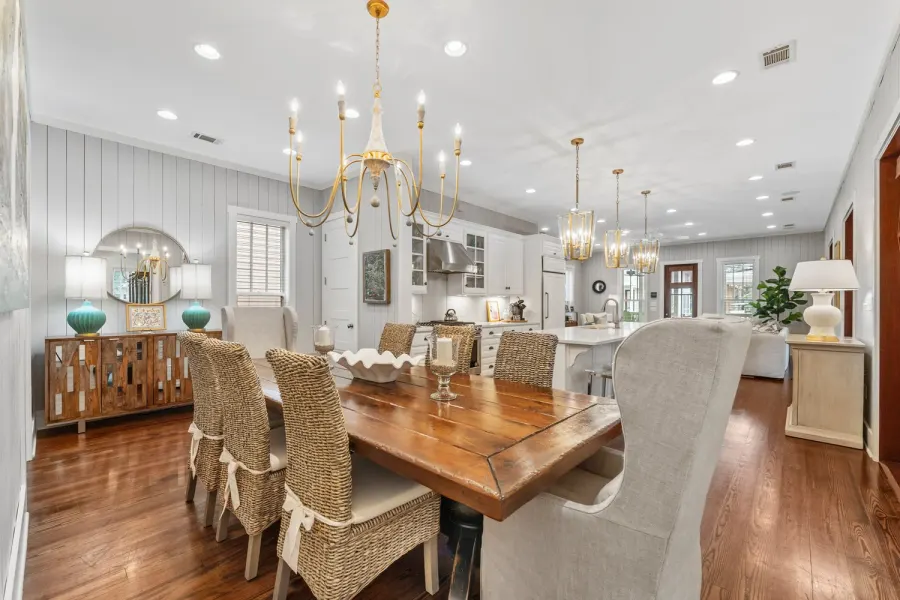 Open dining area with farmhouse table, woven chairs, and brass chandeliers