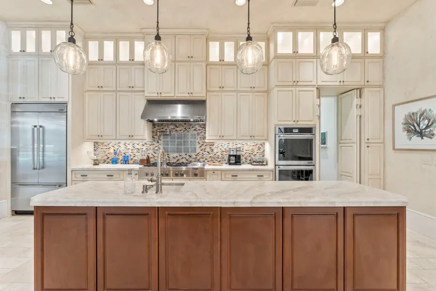 Cream kitchen with large marble island, glass pendants, and mosaic backsplash
