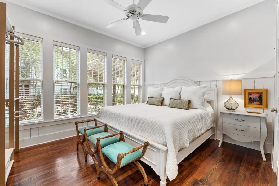 Cottage bedroom with white quilted bed, turquoise benches, and wooded views