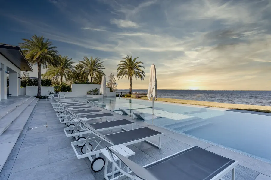 Infinity-edge pool with palm trees and loungers overlooking the Gulf at sunset