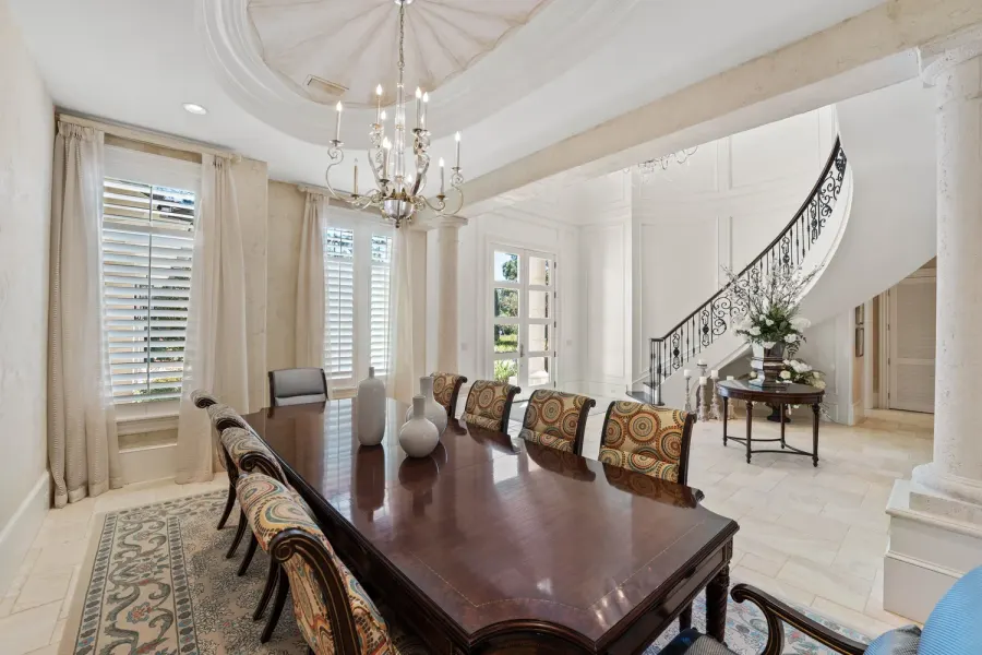 Formal dining room with long wood table, chandelier, and curved iron staircase beyond