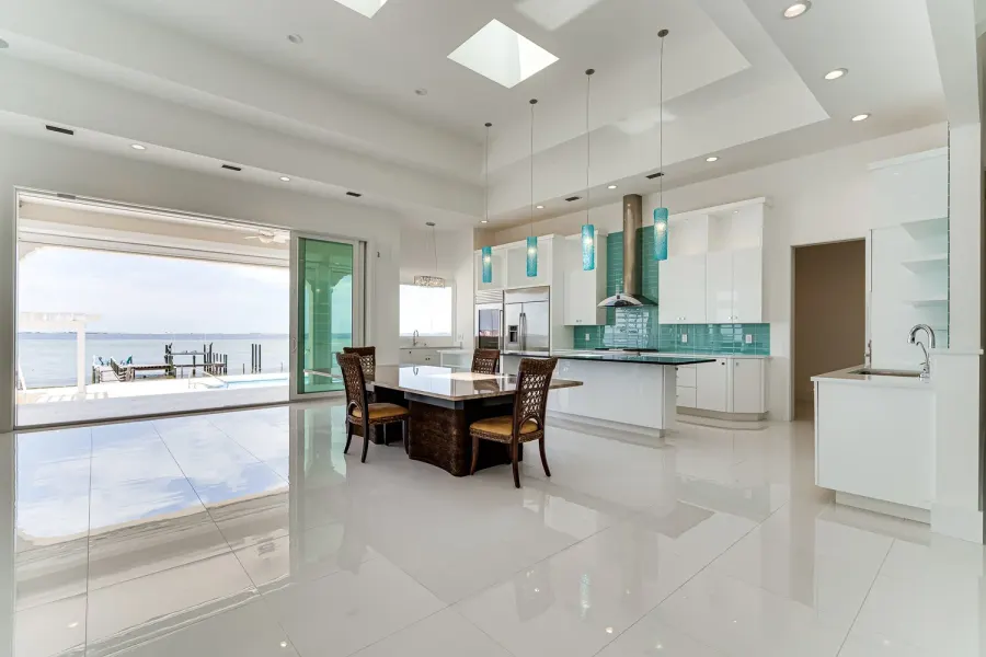 Open white kitchen with aqua glass pendants and sliding doors to a Florida bayfront pool