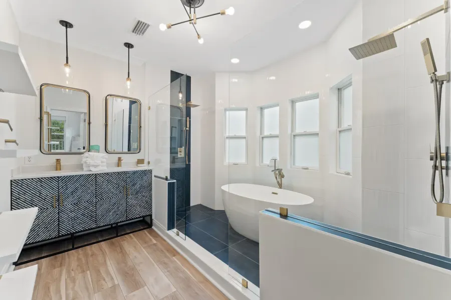 Modern bathroom with freestanding tub, glass showers, and navy tile accents