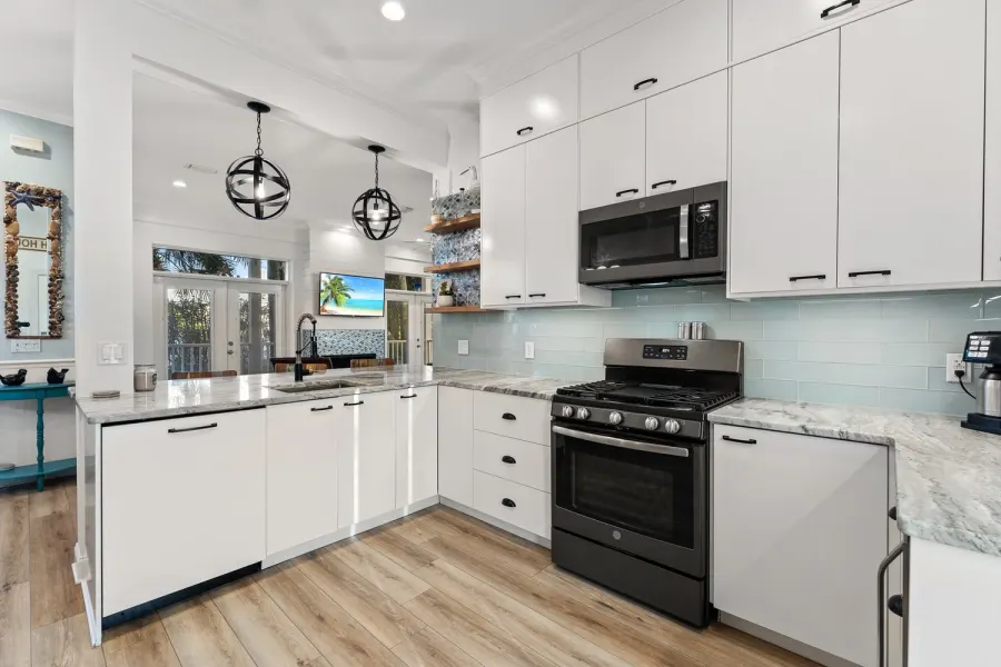 White kitchen with marble counters, sea glass backsplash, and gas range