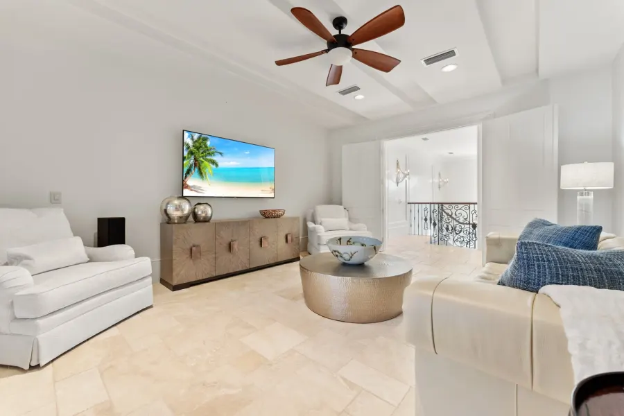 Coastal living room with white sofas, ceiling fan, and travertine floors
