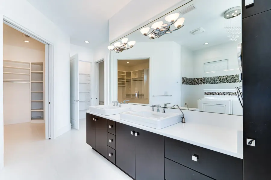 Modern double vanity bathroom with dark cabinets and walk-in closet