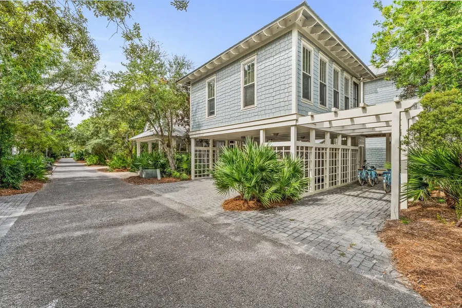Blue shingle-sided beach cottage with pergola carport in a wooded Florida neighborhood
