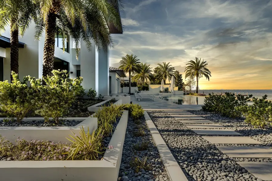 Modern gulf-front estate walkway with palms at golden sunset