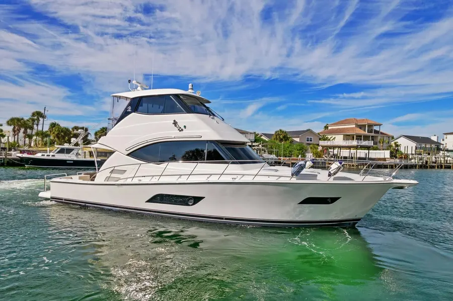 White enclosed-bridge yacht cruising a harbor lined with beach houses