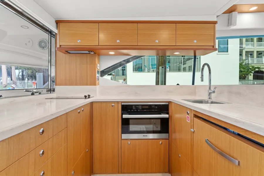 Teak yacht galley with wall oven, sink, and dockside window views