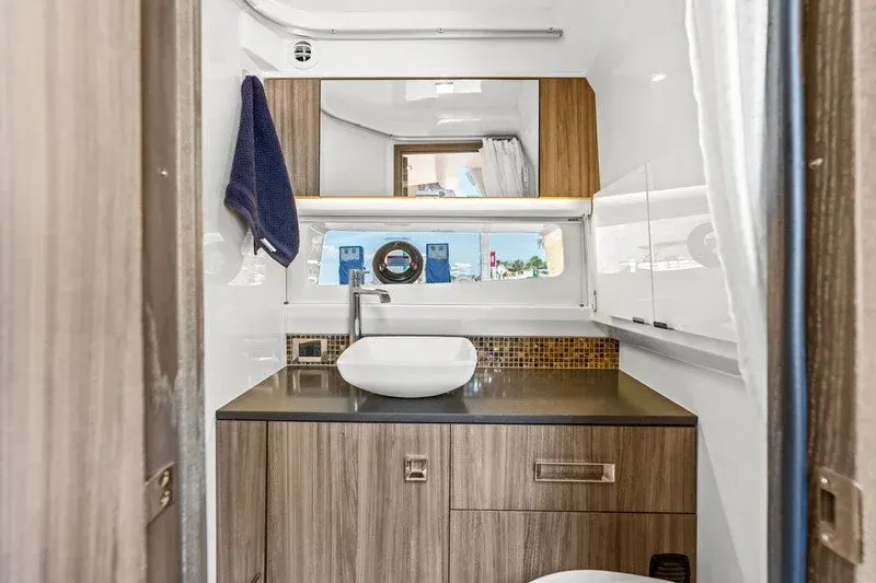 Compact yacht head with vessel sink, mirrored cabinet, and porthole window