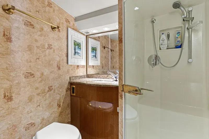 Yacht bathroom with glass shower, granite vanity, and tropical wallpaper