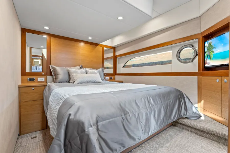 Guest stateroom with satin bedding, teak paneling, and porthole window
